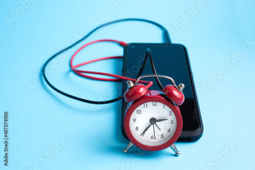 Mobile phone and clock connected with red and black wires, conceptual set as a external alarm clock. 