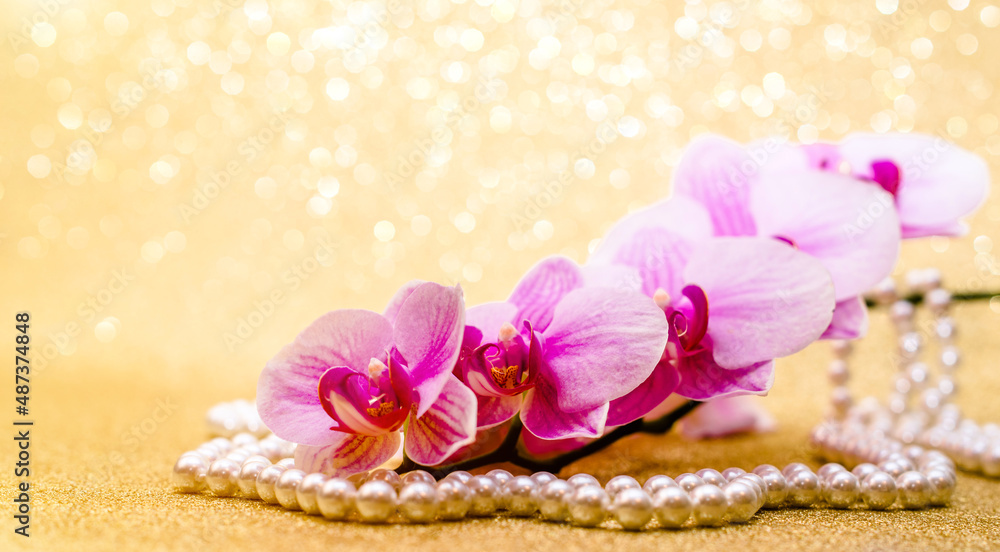 purple Orchid and pearl necklace on a shiny gold background
