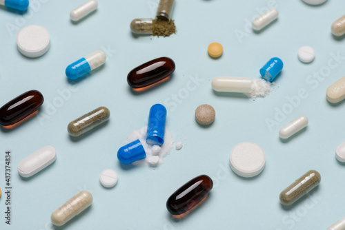 Pills pattern with some capsules open and drug content spilled on blue background