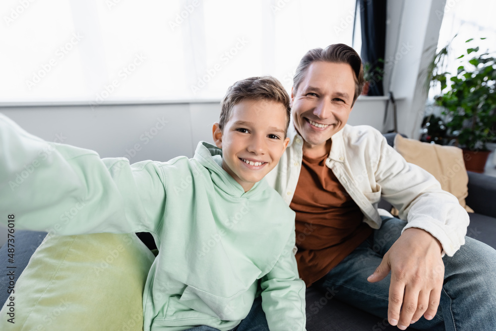 Cheerful boy and man looking at camera while sitting on couch at home Cheerful boy and man looking at camera while sitting on couch at home