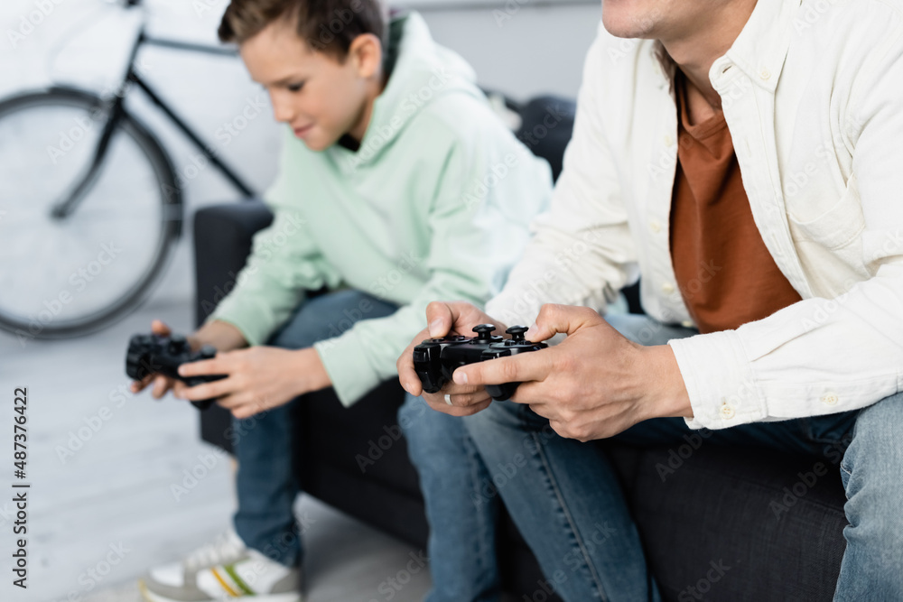 KYIV, UKRAINE - OCTOBER 11, 2021: Man with joystick playing video game near blurred kid at home KYIV, UKRAINE - OCTOBER 11, 2021: Man with joystick playing video game near blurred kid at home