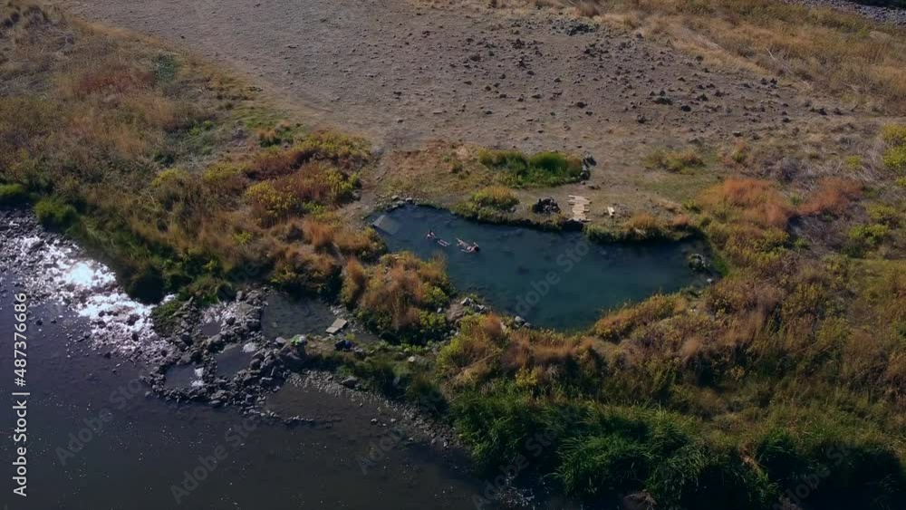 couple relaxes in hot spring pool together on river with aerial view drone shot circle couple relaxes in hot spring pool together on river with aerial view drone shot circle