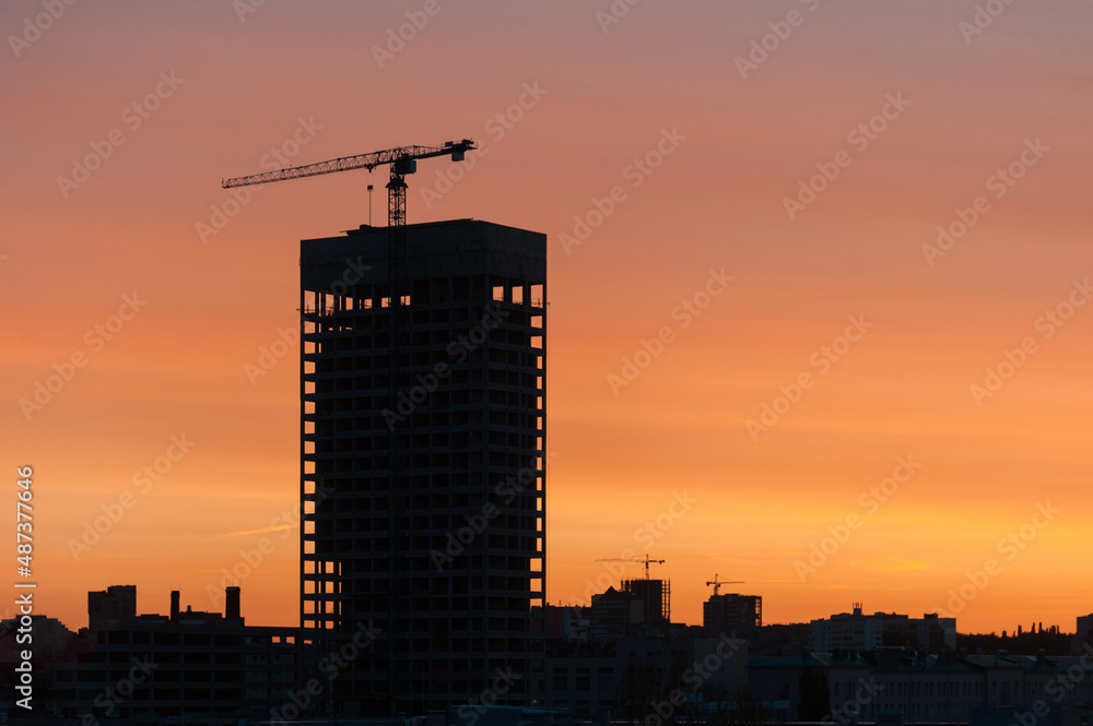 Construction crane together with a new skyscraper during construction against the backdrop of sunset.