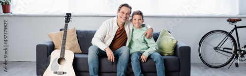 Cheerful father hugging son near acoustic guitar at home, banner