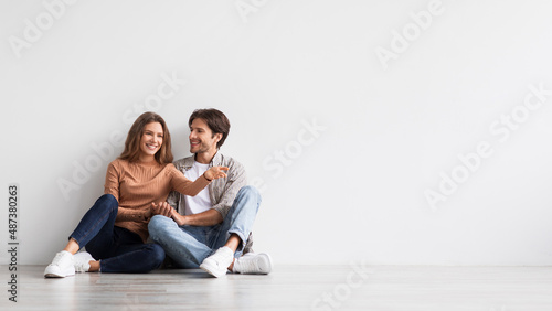 Glad young european man and lady planning future interior in first home, dream, sit on floor on white wall background