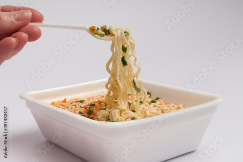 chinese noodles with vegetables and spices on a fork in a human hand. fast food concept