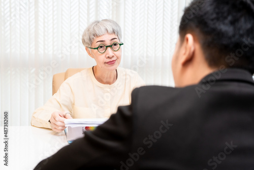 Fototapeta Naklejka Na Ścianę i Meble -  male job applicant Asians are Interview with an elderly Asian woman manager in an office in a friendly atmosphere. The interviewees were very satisfied with the qualifications of the job applicants.