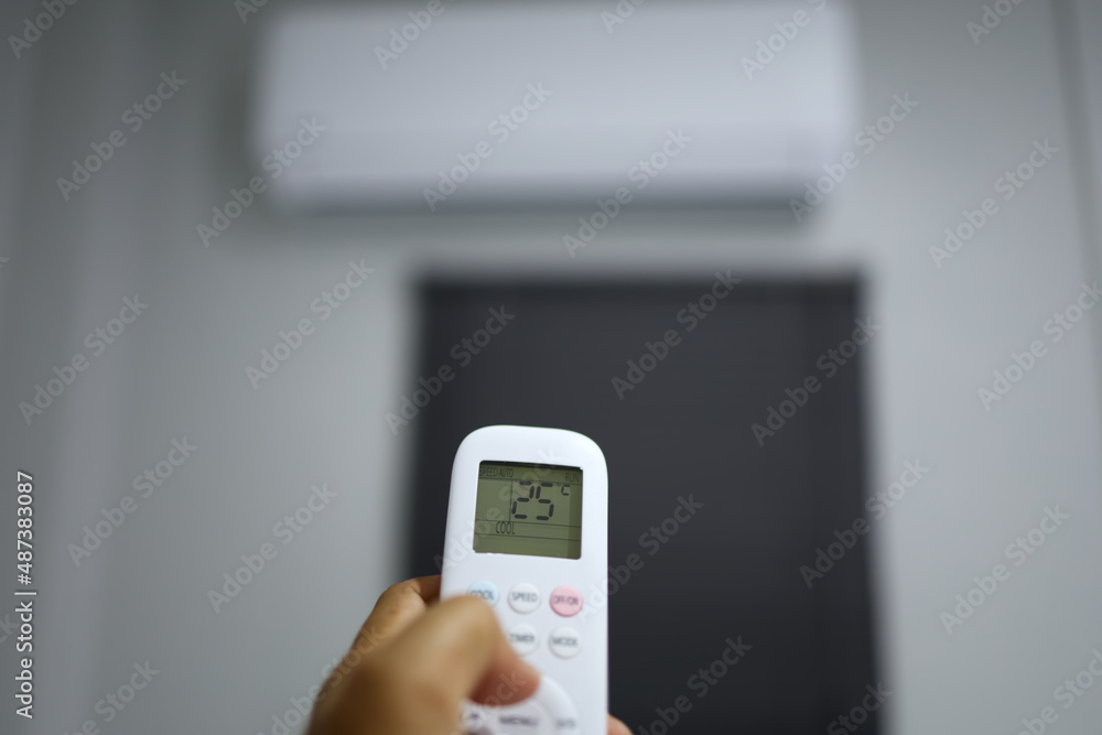 The user of the air conditioner is using the hand to press the remote control to adjust the operating temperature of the air conditioner during use. The user of the air conditioner is using the hand to press the remote control to adjust the operating temperature of the air conditioner during use.