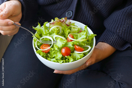 Woman eating holding salad bowl, top view. Girl in sitting holding plate with hands visible, top view.Clean eating, dieting, vegan food concept.