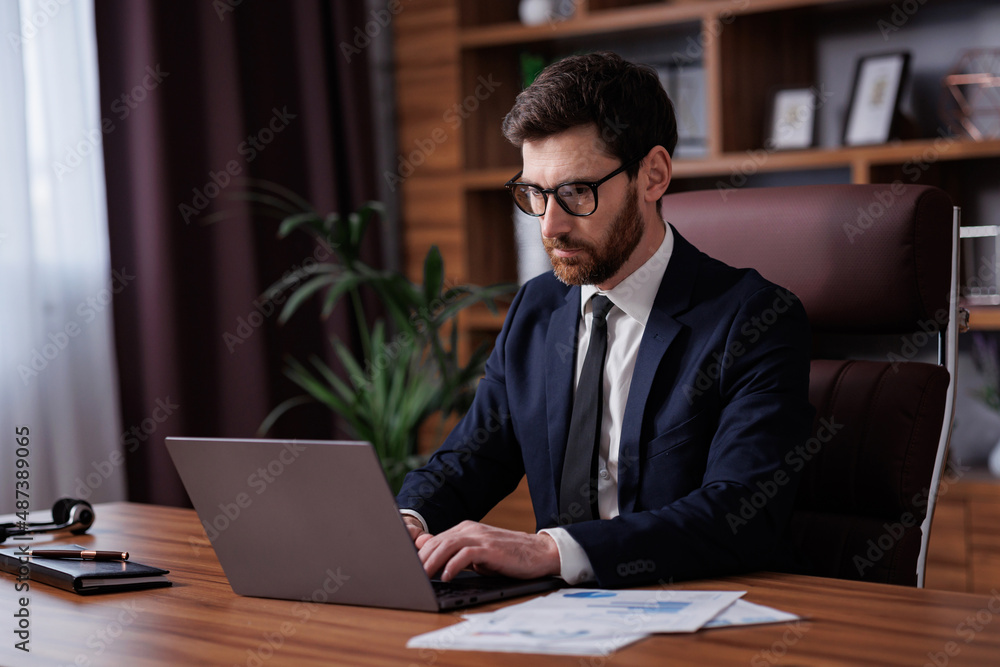 Man portrait in cinematographic light. Handsome businessman is working in the office. Work behind a laptop analysis of data and graphs Man portrait in cinematographic light. Handsome businessman is working in the office. Work behind a laptop analysis of data and graphs