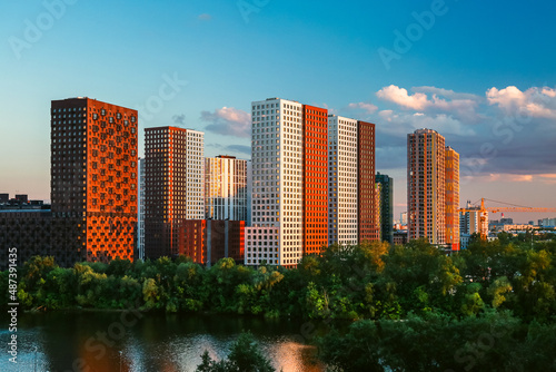 Modern residential area on river bank in Europe. Beautiful view of white and red high-rise multi-storey buildings in sunshine.