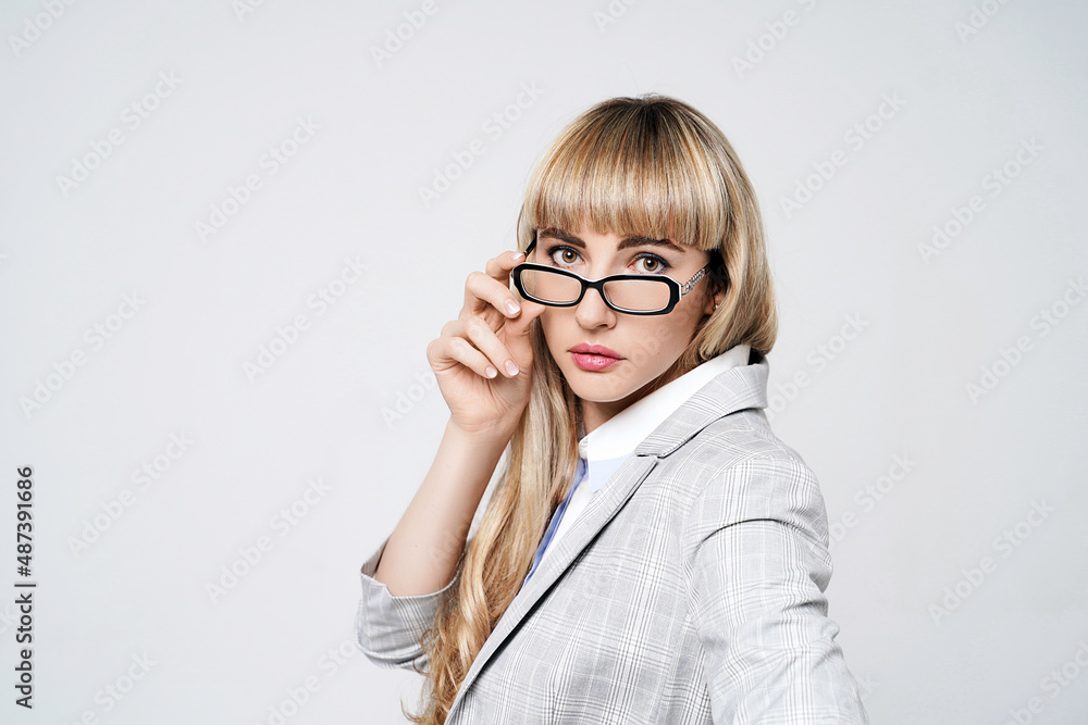 Closeup portrait of young beautiful blonde woman in studio on light gray background. Model in pantsuit and glasses.