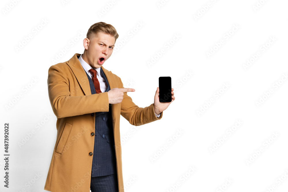 Portrait of young businessman, student, elegant man wearing suit and beige coat using phone isolated on white studio background.