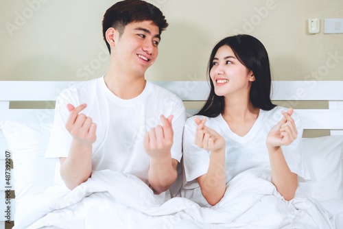 Happy couple relaxing show hand in shape of heart on bed in bedroom.