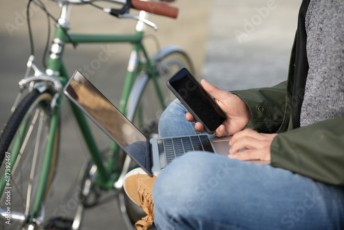 Closeup of man using phone and laptop beside classic bicycle