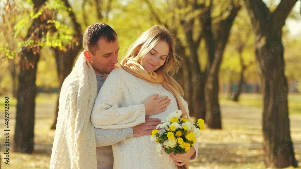 Pregnant woman and man in warm knitted sweaters hug at sunny warm autumn park Pregnant woman and man in warm knitted sweaters hug at sunny warm autumn park