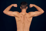 Handsome young man isolated. Portrait of shirtless muscular man is standing on grey background and showing his biceps. Back view