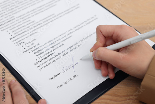 Woman signing contract at wooden table, closeup.