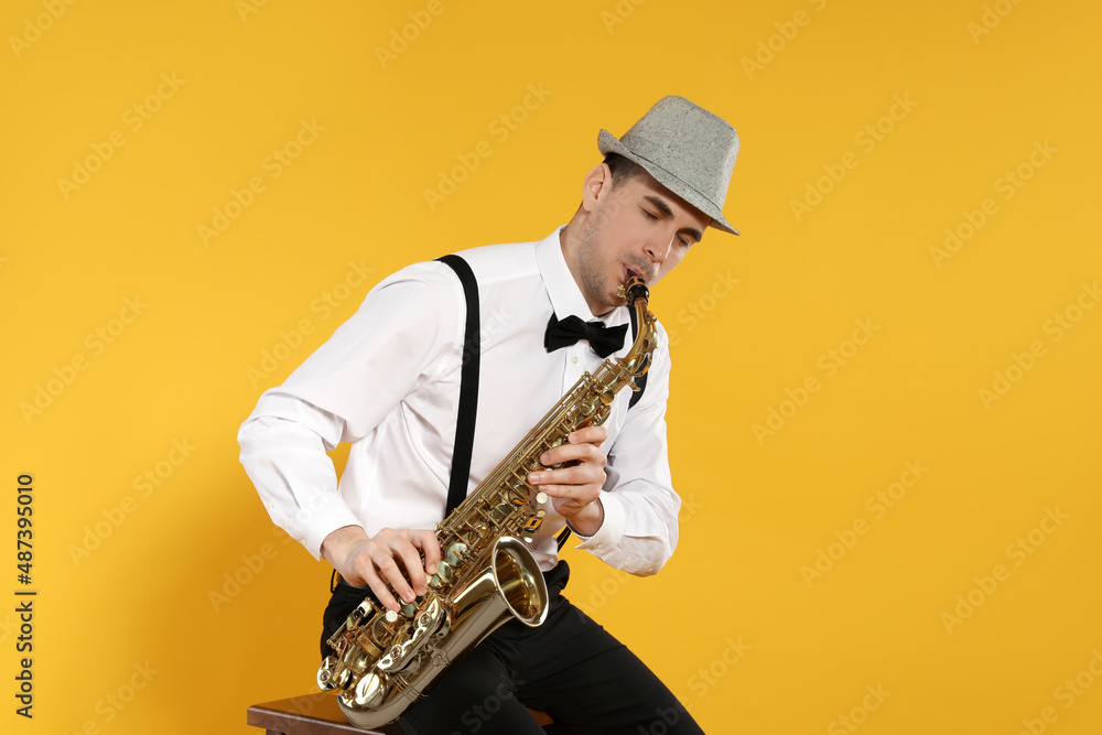 Naklejka premium Young man in elegant outfit playing saxophone on yellow background