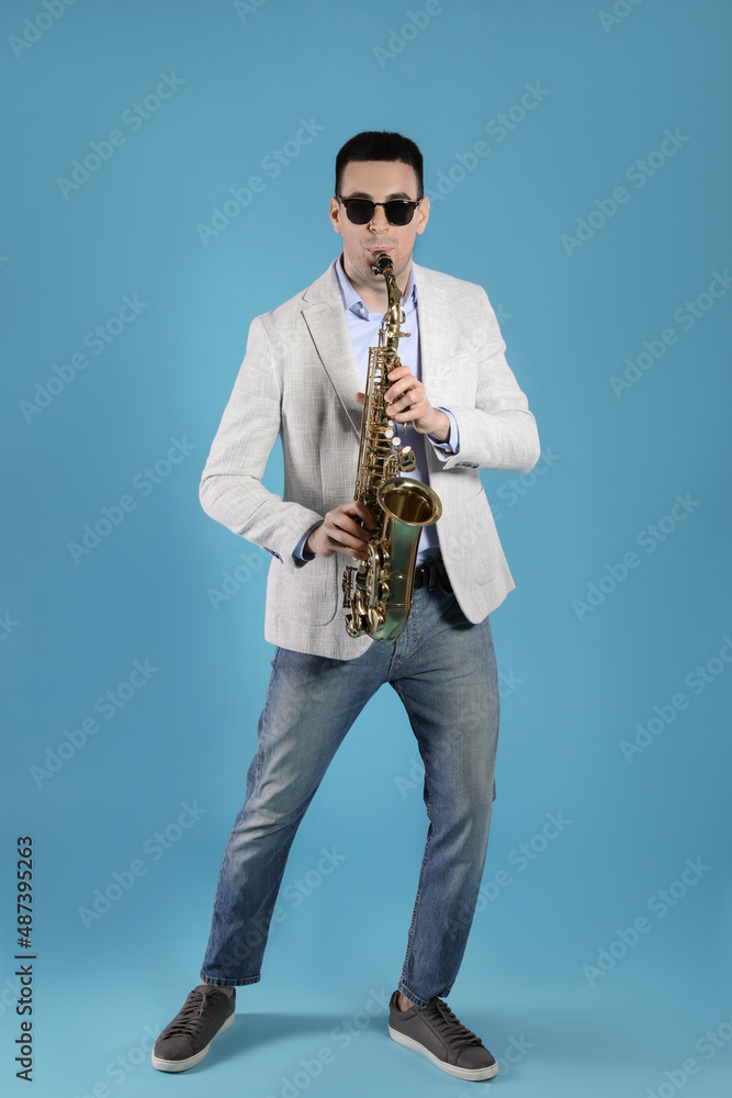 Naklejka premium Young man playing saxophone on light blue background