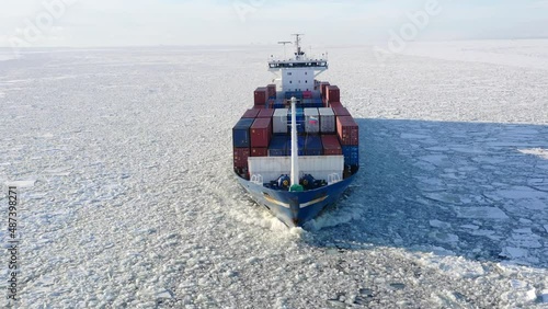 St. Petersburg, Russia, winter 2022: aerial view Cargo container ship running through the ice floe, front side of the ship. Ice floes brakes on side of ship