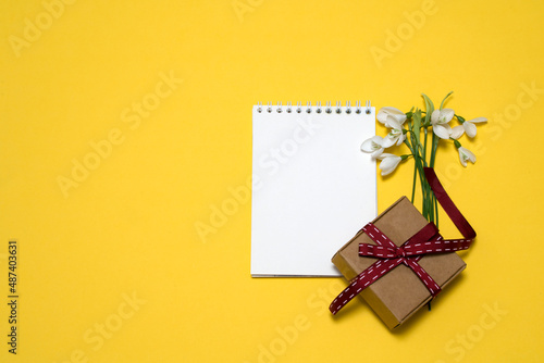 on a yellow background a bouquet of snowdrops, a notebook, a gift box. card, congratulations on March 8