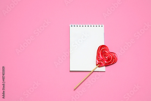 on a bright pink background a red lollipop in the shape of a heart, a sheet for notes. card, congratulations on Valentine's Day. romantic background. place for text