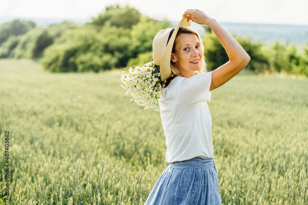 Obraz premium Summer Lifestyle Concept. Trendy adult woman in stylish summer dress feeling free in the field with wild flowers in sunshine.