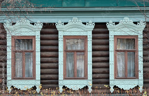 The old window of a rustic Russian wooden house is richly decorated with carvings in an old Russian city.