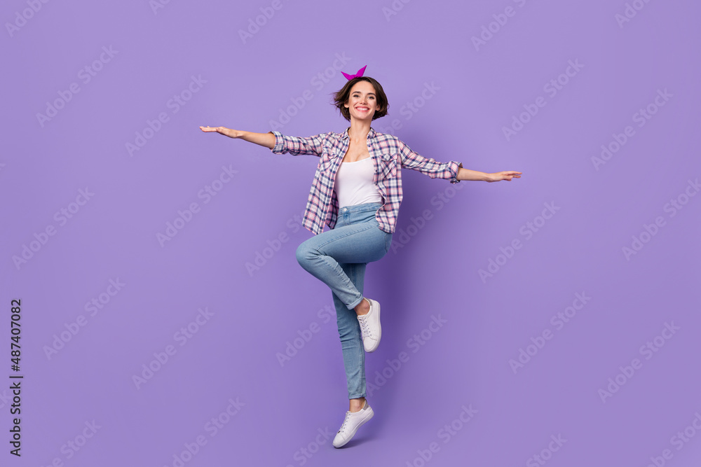 Photo of sweet pretty woman wear plaid shirt jumping high arms sides isolated violet color background Photo of sweet pretty woman wear plaid shirt jumping high arms sides isolated violet color background