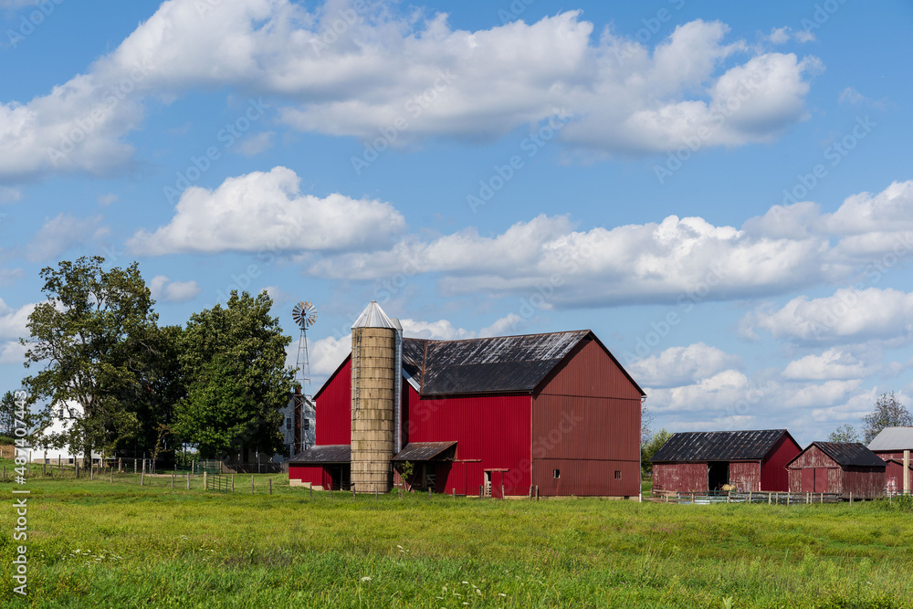 Red Barn with Silo amidst a Green Hay Field Under a Partly Cloudy Blue Sky