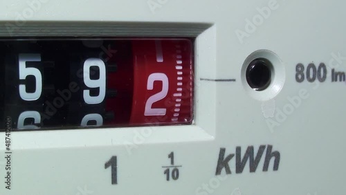 Macro close-up of a household electric meter showing the red dial number moving, kWh symbol. Concept for energy, higher bills, price rise, meter reading, cost of living and electricity supplier.  photo
