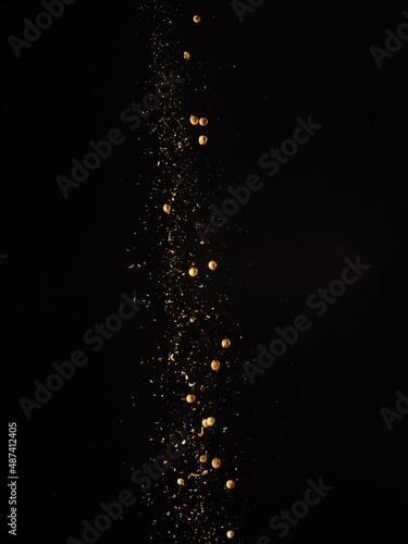 A stream of golden colored spices in a frozen flight isolated on a black background. Abstraction. Minimalism. Spices and seasonings, cooking, supermarket, advertising, banner.