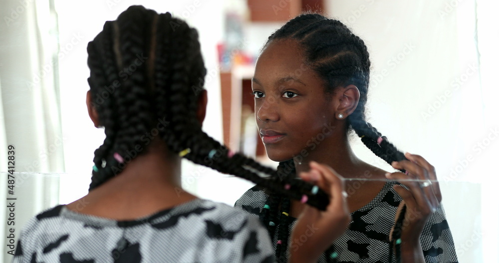 Teenager black girl looking at herself in mirror. Adolescent african girl inspecting face
