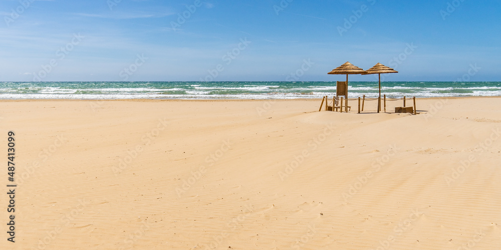 Zwei Sonnenschirme aus Naturfaser einsam auf Sandstrand stehend