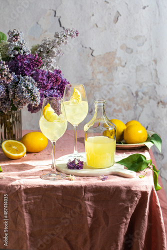 A bottle of Italian traditional liqueur limoncello with glasses, lemons and a vase with blooming lilac