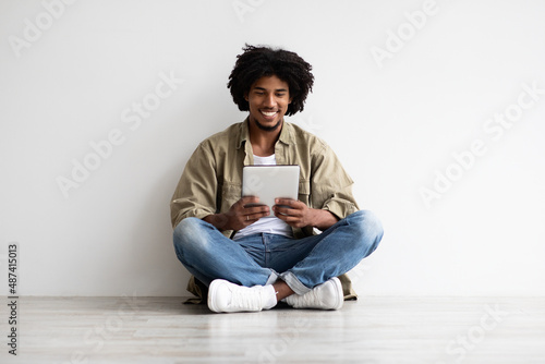 Cheerful Millennial Black Guy With Digital Tablet Relaxing On Floor Indoors © Prostock-studio