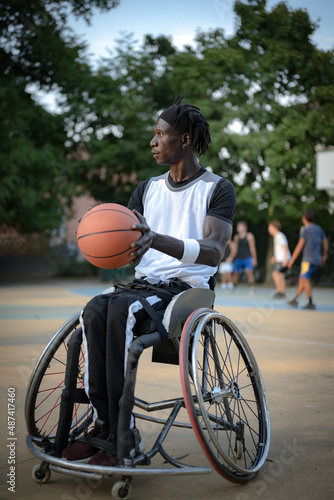 vertical picture of African athlete with a disability caused by polio playing basketball, using professional wheelchair on the ground, concept of determination and mental toughness, accessibility