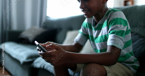 Child holding smartphone device. Mixed race black african boy kid using cellphone at home