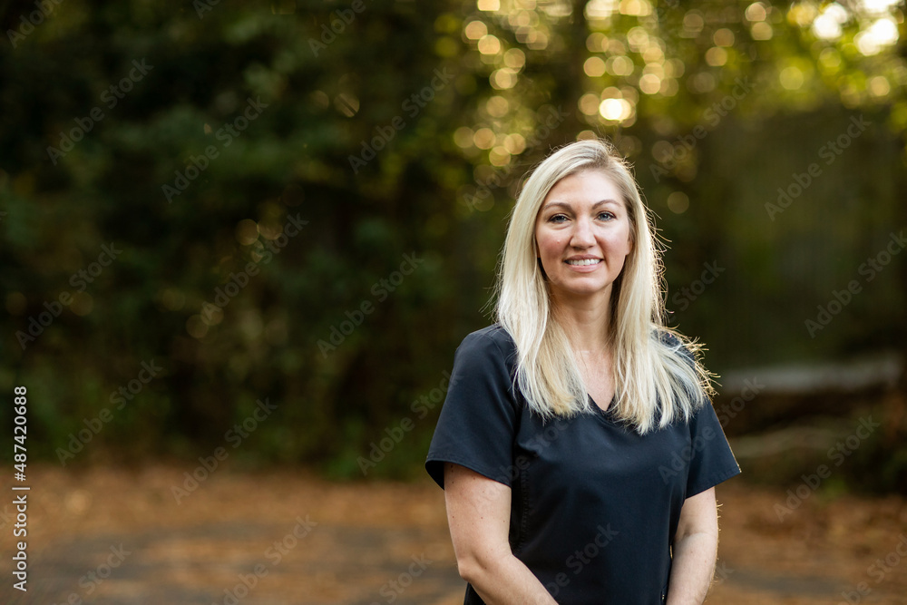 A medical professional with black scrubs with long blond hair outside in a natural background with copy space A medical professional with black scrubs with long blond hair outside in a natural background with copy space