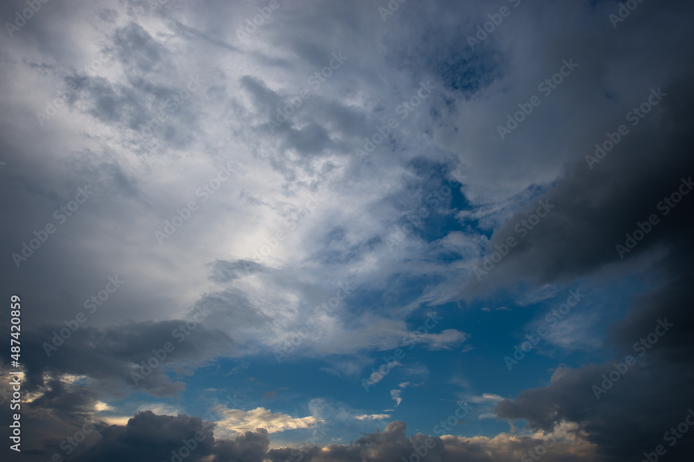 Overhanging dark lead and heavy clouds along with white and orange clouds surround the blue sunset sky Overhanging dark lead and heavy clouds along with white and orange clouds surround the blue sunset sky