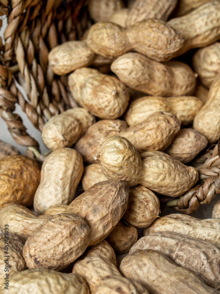 Shelled peanuts in a small wicker basket on a white background. Peanuts full from a wicker basket. Peanuts spill out of a wicker basket. Shelled peanuts in a small wicker basket on a white background. Peanuts full from a wicker basket. Peanuts spill out of a wicker basket.