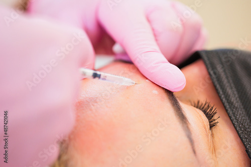 The doctor makes an injection of Botox filler in the patient forehead for the treatment of age wrinkles - age-related skin correction