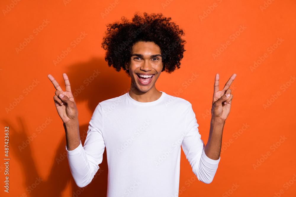 Photo of excited sweet guy dressed white shirt smiling showing two v-signs isolated orange color background Photo of excited sweet guy dressed white shirt smiling showing two v-signs isolated orange color background