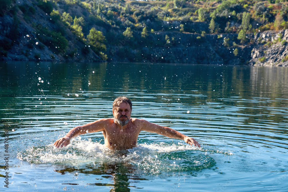 An elderly man swims with great pleasure in a flooded quarry early in the morning. An elderly man swims with great pleasure in a flooded quarry early in the morning.