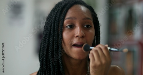 African black teen girl applying make-up in front of mirror