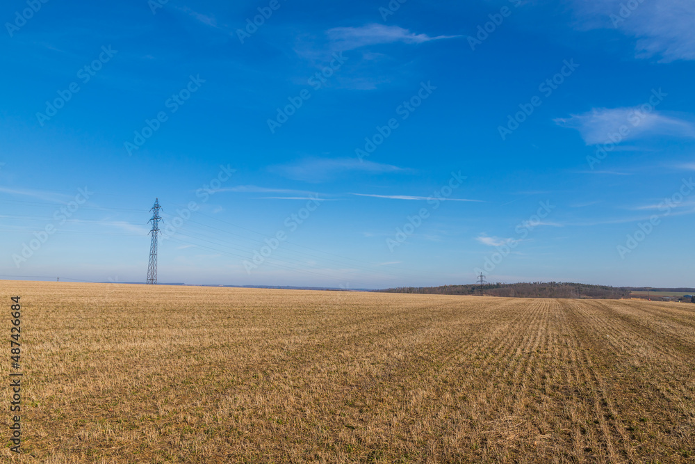 Obraz premium High voltage poles for electricity distribution in the countryside. In the background is a blue sky with dramatic clouds.