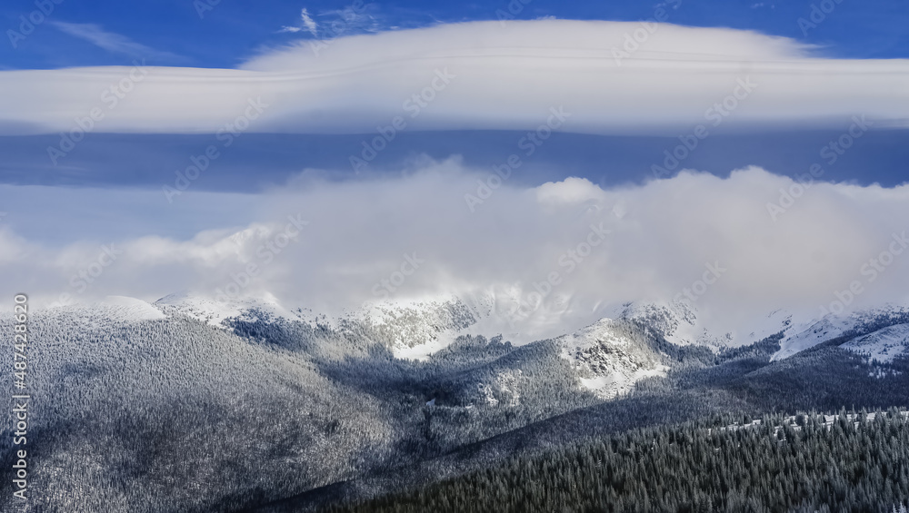 Beautiful panoramic view of Colorado mountain range with ski bowl covered with clouds; blue sky and large cloud formation in background