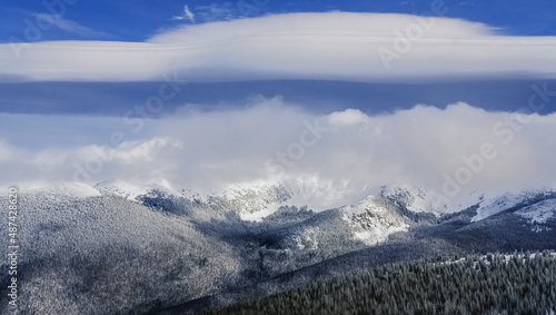 Beautiful panoramic view of Colorado mountain range with ski bowl covered with clouds  blue sky and large cloud formation in background © Lana
