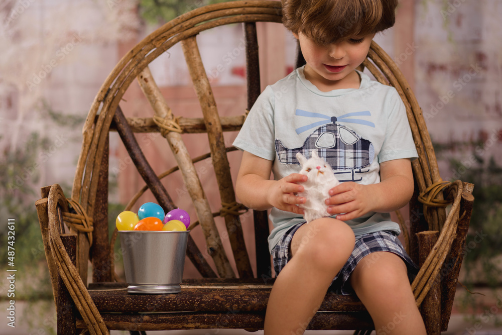 Naklejka premium little boy petting a bunny for Easter in a wooden chair 